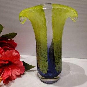 May include: A green and blue glass vase with a unique, wavy design. The vase has a clear glass base and a textured, speckled finish.