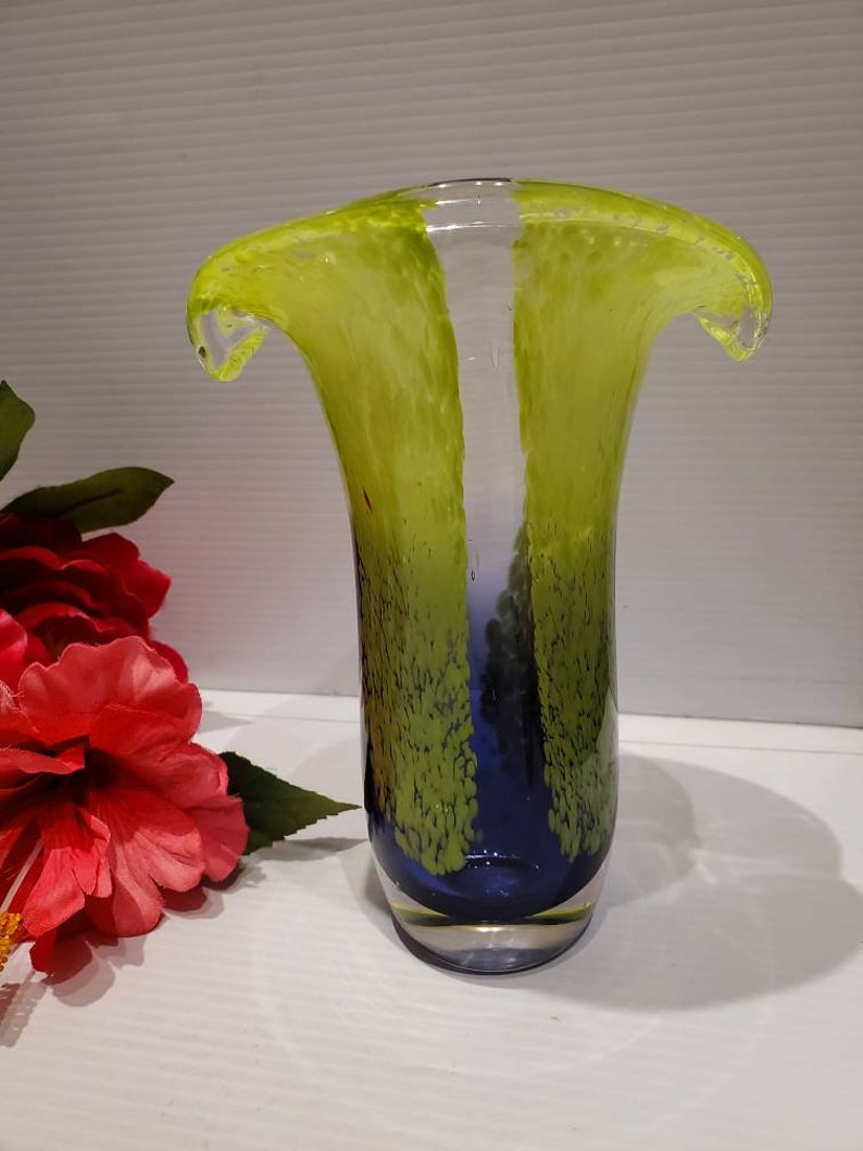 May include: A green and blue glass vase with a unique, wavy design. The vase has a clear glass base and a textured, speckled finish.