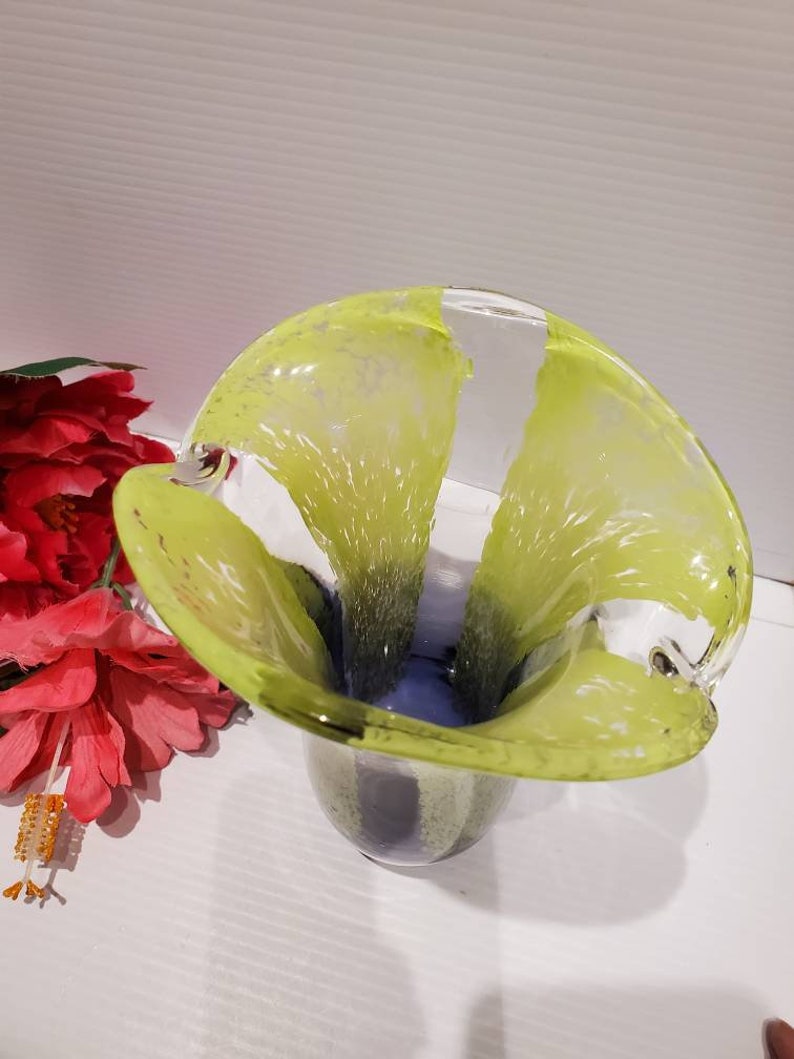 May include: A green and blue glass vase with a unique, wavy design. The vase has a wide opening and a narrow base.