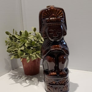 May include: A brown ceramic figurine of a person wearing a headdress. The figurine is sitting on a base with the word "Kuala" written on it.