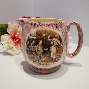 Może przedstawiać: Dzbanek ceramiczny w kolorze różowym i brązowym z nadrukowaną sceną z Olivera Twista, "Oliver Twist prosi o więcej". Dzbanek ma uchwyt i fakturowaną powierzchnię.