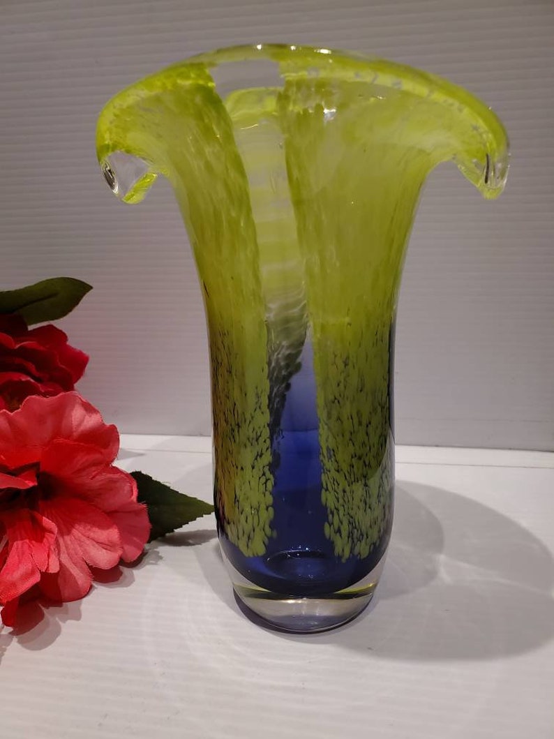 May include: A glass vase with a wide, flared opening and a narrow base. The vase is made of clear glass with a blue and green swirl pattern.