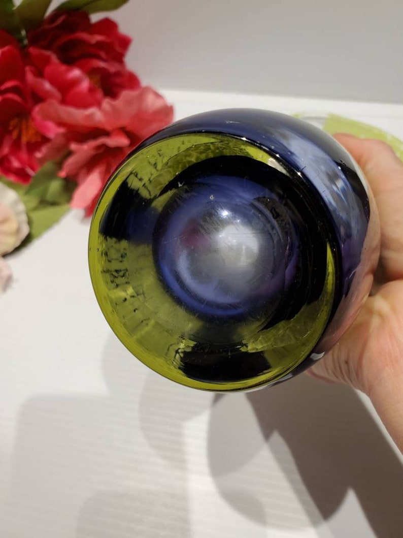May include: A dark blue glass bottle with a yellow rim. The bottle is round and has a smooth surface.
