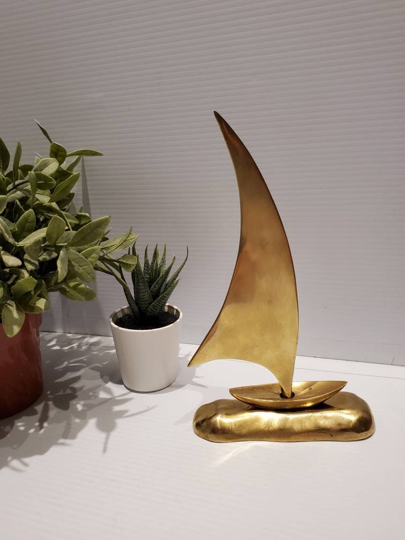 May include: A gold-colored metal sculpture of a sailboat with a single sail. The sailboat is sitting on a base that resembles a wave.