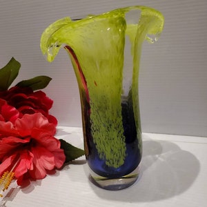 May include: A green and blue glass vase with a wavy, ruffled top. The vase has a speckled, textured surface.