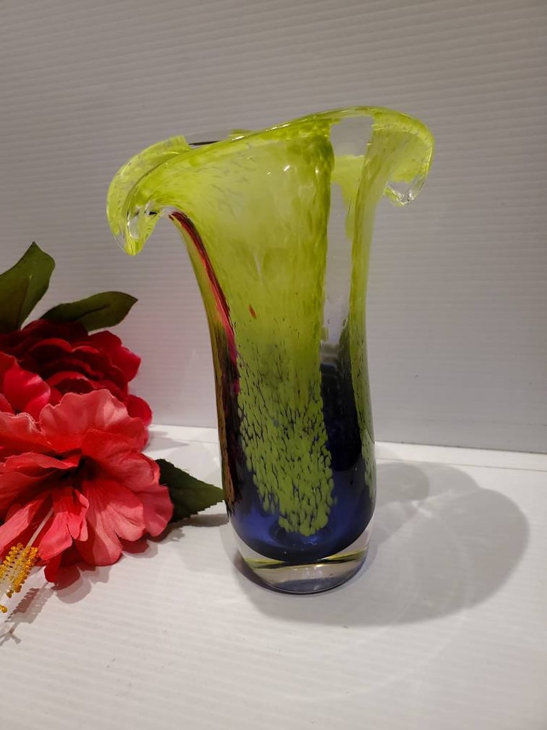 May include: A green and blue glass vase with a wavy, ruffled top. The vase has a speckled, textured surface.
