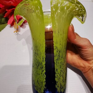 May include: A tall, green and blue glass vase with a unique, wavy design. The vase has a textured surface with small white dots.