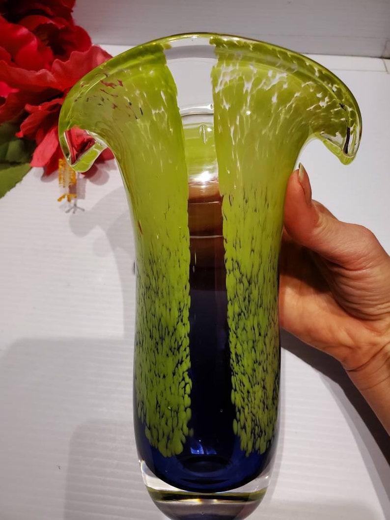 May include: A tall, green and blue glass vase with a unique, wavy design. The vase has a textured surface with small white dots.