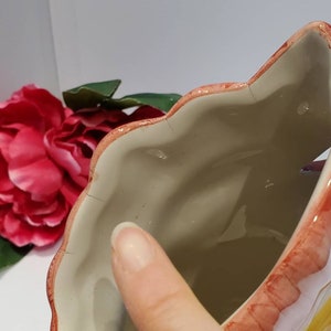 May include: A ceramic planter shaped like a flower with a pink and white glaze. The planter has a scalloped edge and a wide opening.
