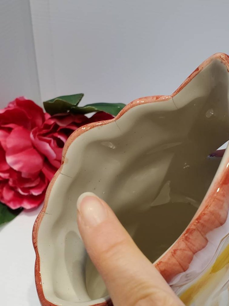 May include: A ceramic planter shaped like a flower with a pink and white glaze. The planter has a scalloped edge and a wide opening.