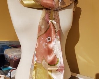 May include: A long, flowing scarf with a colourful abstract floral pattern in shades of pink, green, and gold. The scarf is made of a sheer fabric with a satin trim.
