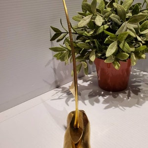 May include: A gold-colored metal sculpture of a sailboat with a long, thin mast and a triangular sail. The sculpture is on a base that resembles a wave.