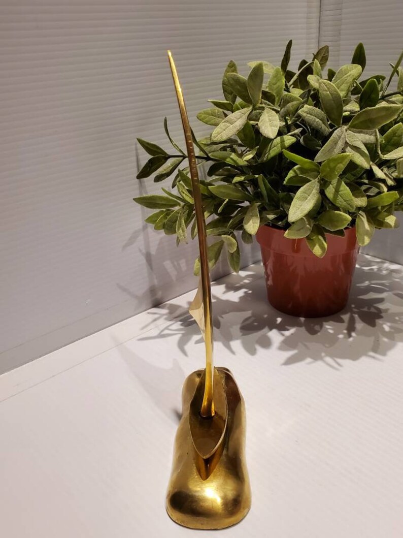May include: A gold-colored metal sculpture of a sailboat with a long, thin mast and a triangular sail. The sculpture is on a base that resembles a wave.