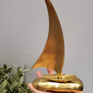 May include: A gold-colored brass sailboat sculpture with a single sail. The sailboat is sitting on a base that resembles a wave.