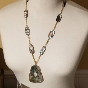 May include: A gold chain necklace with a large, iridescent, green and brown shell pendant. The necklace features smaller, oval-shaped shell beads.