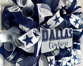 May include: A blue and white Dallas Cowboys wreath with a sign that says "Dallas Cowboys". The wreath is made of mesh and ribbon and features silver glitter stars.