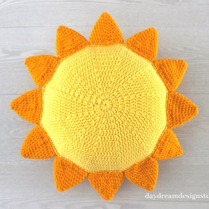 May include: A crocheted sun pillow with yellow and orange yarn. The pillow is shaped like a sun with a round center and 12 points.
