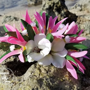 May include: Pink and white flower lei with green leaves. The lei is made of silk flowers and is perfect for a luau or other tropical event.
