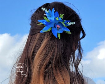May include: A blue orchid hair clip with green leaves. The clip is worn in a woman's brown hair.