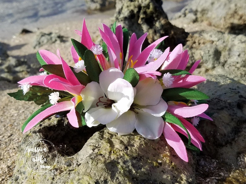 May include: Pink and white flower lei with green leaves. The lei is made of silk flowers and is perfect for a luau or other tropical event.