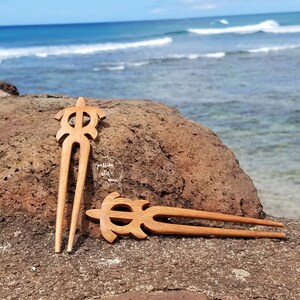 May include: Two wooden hair sticks with a turtle design. The sticks are brown and have a smooth finish. They are lying on a brown rock with a blurred background of the sea.