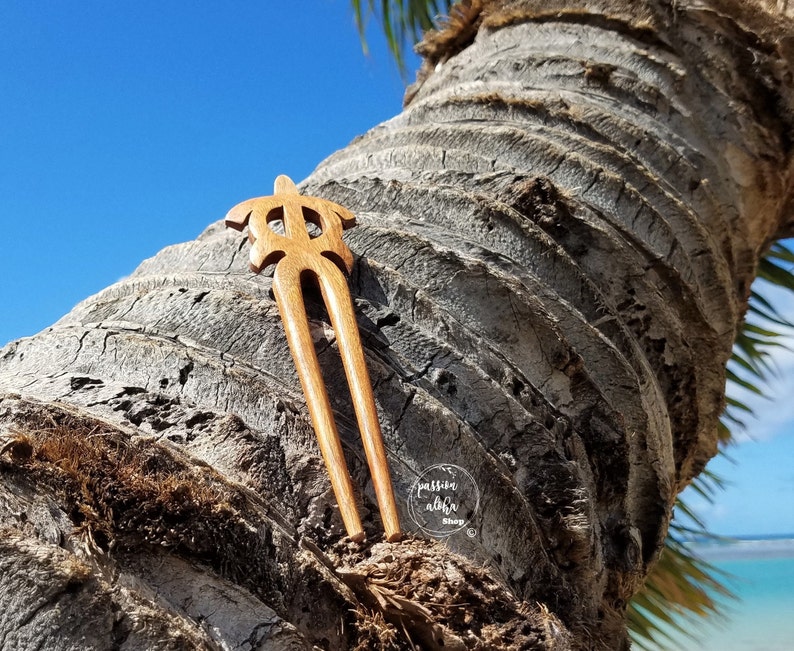 May include: A wooden hair fork with a turtle design. The fork is brown and has two prongs. It is resting on a tree trunk.