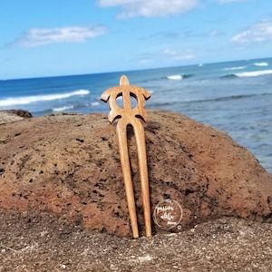 May include: Wooden hair fork with a turtle design. The fork is brown and has a natural finish. It is sitting on a rock with the ocean in the background. The text "passion aloha shop" is visible in the lower right corner of the image.