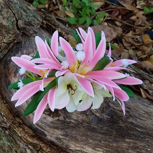 May include: A pink and white flower hair clip with green leaves. The flower is made of fabric and has a realistic appearance.