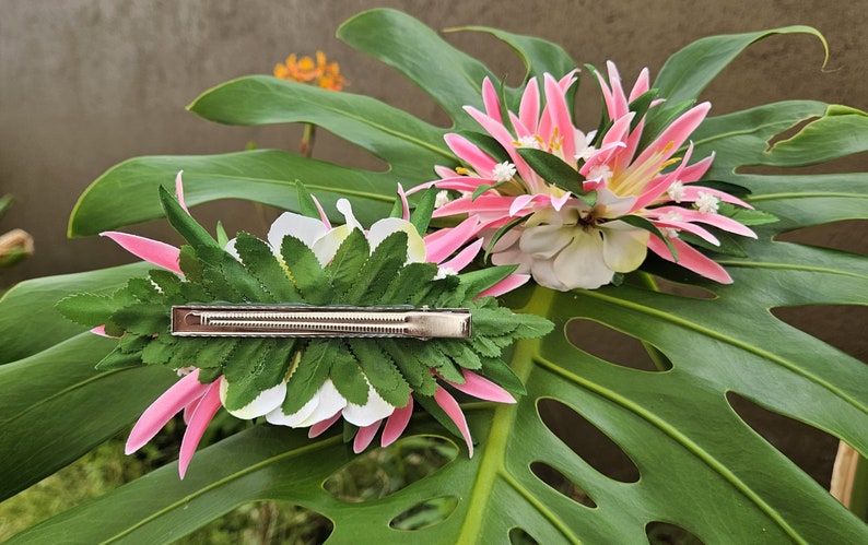 May include: Two pink and white flower hair clips with green leaves. The clips have a silver metal bar.