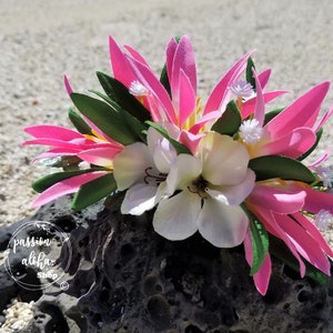 May include: Pink and white flower crown with green leaves. The crown is sitting on a dark gray rock.