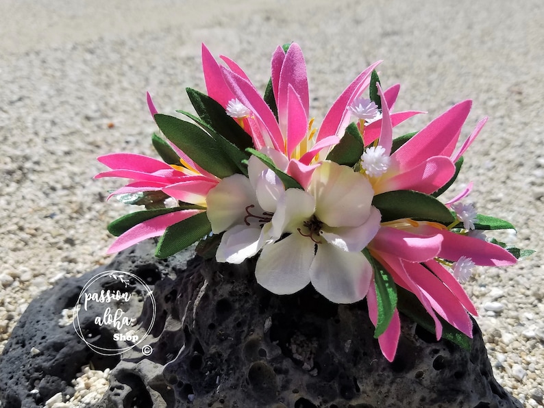 May include: Pink and white flower crown with green leaves. The crown is sitting on a dark gray rock.
