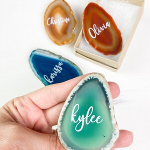 May include: Four agate slices with names written on them in white lettering. The names are "Olivia", "Christian", "Kyler", and "Korissa".