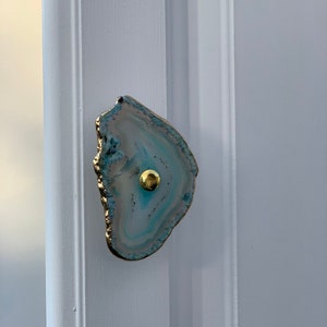 May include: A light blue agate door knob with a gold metal accent. The knob is mounted on a white door.