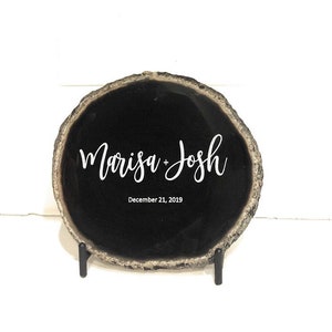 May include: Black agate slice with the names "Marisa + Josh" and the date "December 21, 2019" engraved in white. The slice is on a black metal stand.