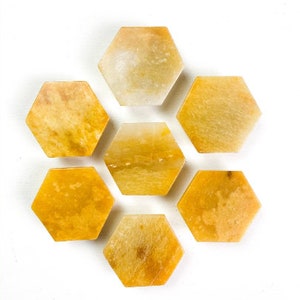 Puede incluir: Siete baldosas hexagonales de piedra amarillo-anaranjada dispuestas sobre una superficie blanca. Las baldosas tienen un aspecto natural veteado con variaciones de color y textura. La disposición sugiere un elemento decorativo o artesanal.
