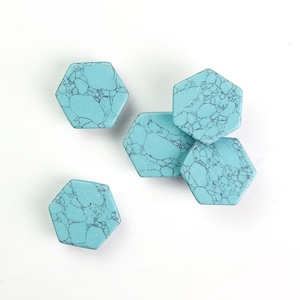 May include: Five hexagonal turquoise stones with a marbled appearance. The stones are a light blue colour with dark grey veining, and are arranged on a white surface. These stones could be used for jewellery making or other craft projects.