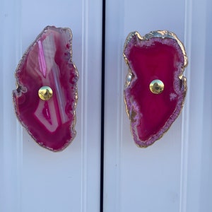May include: Two pink agate drawer pulls with gold trim and a gold knob in the center.