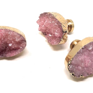 May include: Three pink crystal drawer pulls with gold metal accents. The crystal is a cluster of small pink crystals.