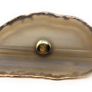 May include: A light brown agate slice with a gold rim and a gold metal knob in the center.