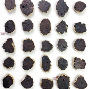 Op de afbeelding: Een verzameling van 25 zwarte en gouden onderzetters. De onderzetters zijn gemaakt van een natuurlijk materiaal, mogelijk steen of agaat, en hebben een ruw, getextureerd oppervlak. Elke onderzetter heeft een dunne gouden rand.