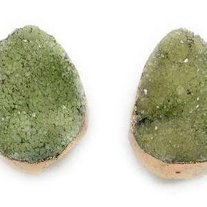 May include: A pair of green agate earrings with a gold rim. The earrings are shaped like a teardrop and have a rough, textured surface.