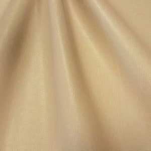 May include: A close-up of a smooth, light beige fabric with a subtle texture. The fabric is draped and folded, creating soft, flowing lines.