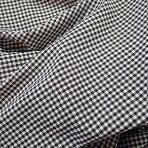 May include: Black and white gingham fabric with a checkered pattern. The fabric is folded and wrinkled.