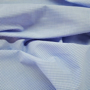 May include: A close-up of a light blue and white gingham fabric. The fabric is folded and wrinkled, showing the texture of the material.