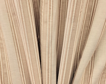 May include: Close-up of a fabric with vertical stripes in shades of beige and light brown. The fabric has a textured appearance with varying widths of stripes, creating a subtle pattern. The folds in the fabric add depth.