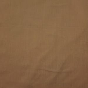 May include: A close-up shot of a tan fabric with a subtle woven texture. The material has a slightly wrinkled appearance, with soft shadows and highlights across its surface. The overall color is a warm, neutral tone.