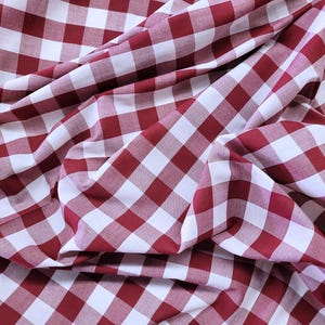 May include: Close-up of a red and white checkered fabric. The fabric is draped and folded, creating shadows and depth. The pattern is a classic gingham design, with evenly spaced squares.