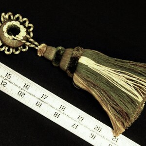 May include: A green and cream tassel with a gold and cream decorative top. The tassel is approximately 7 inches long.