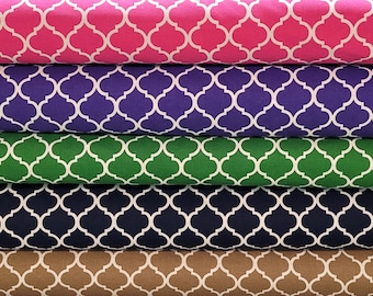 May include: Stacks of fabric in various colors, including pink, purple, green, navy, and tan. Each fabric features a white quatrefoil pattern. The fabrics are neatly folded, showcasing the repeating design.