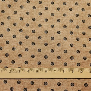 May include: A brown fabric with a repeating pattern of small black circles. A wooden ruler with inch markings is placed on the fabric.